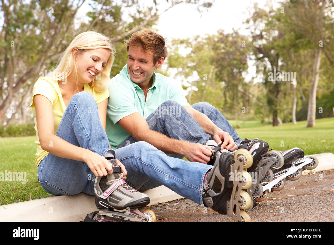 Couple Putting On In Line Skates In Park Stock Photo