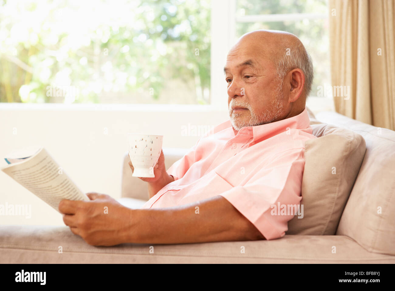 Senior Man Reading Book With Drink At Home Stock Photo