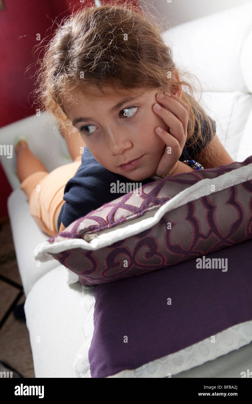 9 years old girl lying on the couch on a bunch of pillow indoors Stock Photo