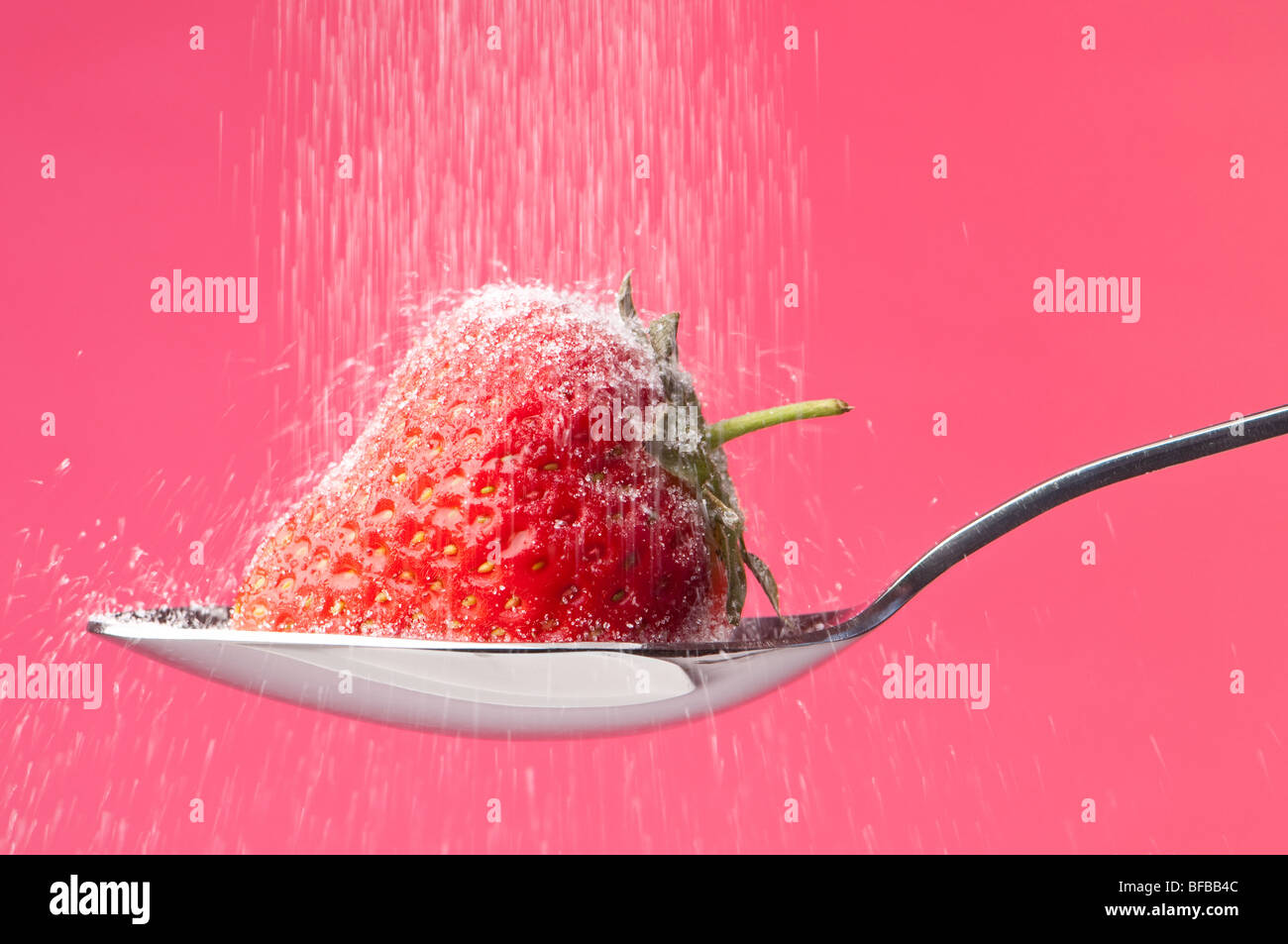 Sugar sprinkling onto strawberry on spoon Stock Photo