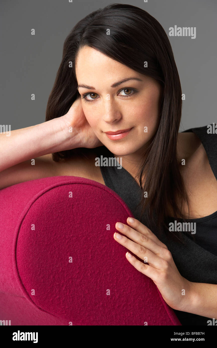Studio Portrait Of Woman Relaxing On Pink Chaise Longue Stock Photo