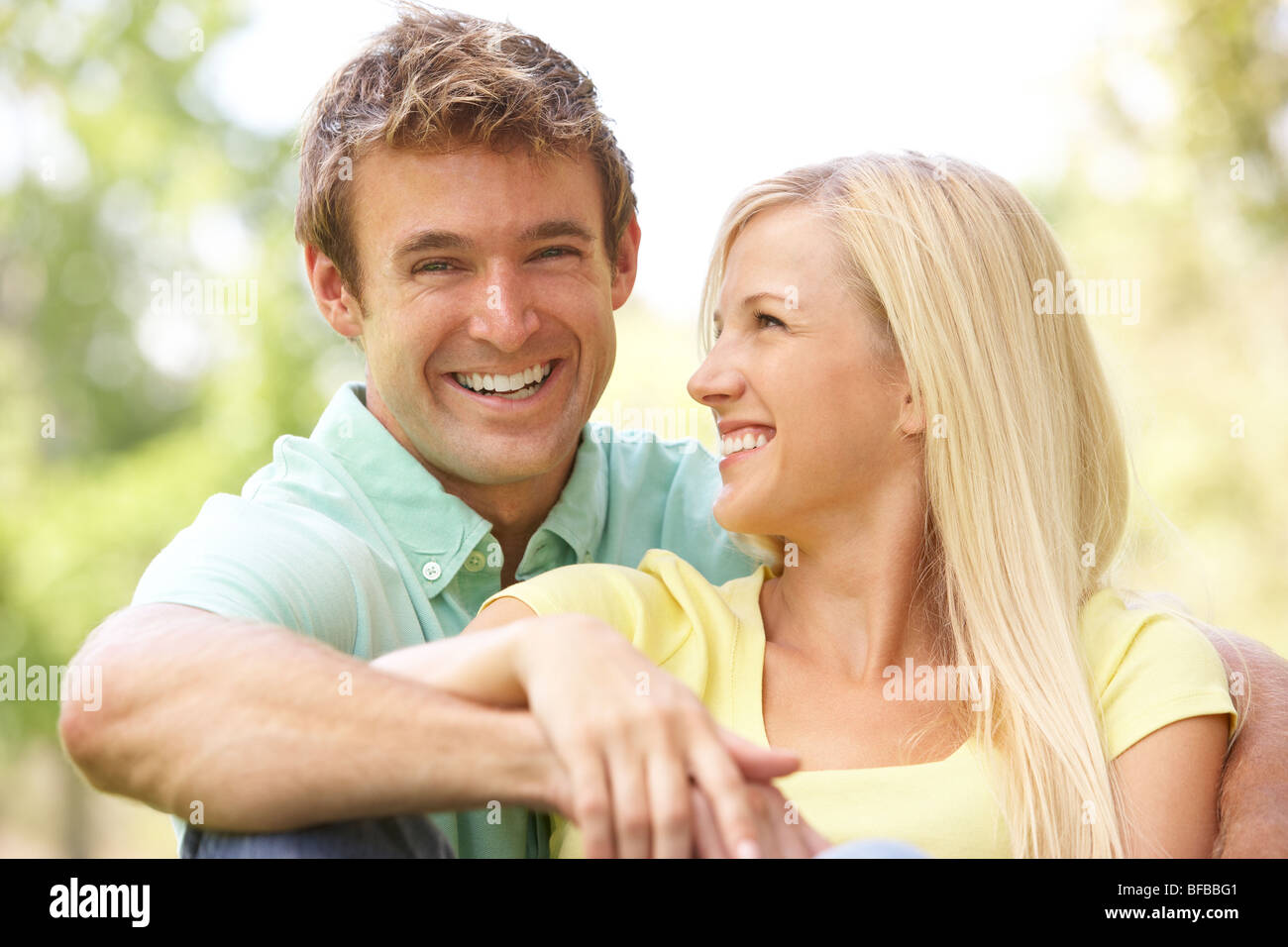 Portrait Of Young Couple Sitting In Park Stock Photo - Alamy