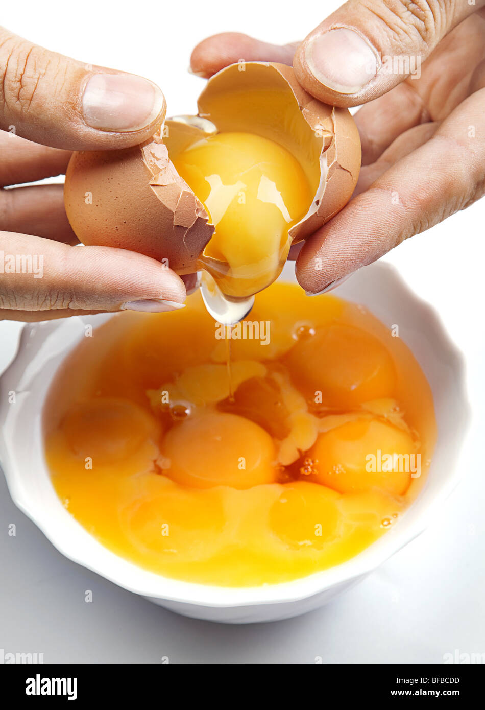 Opening brown egg in white plate with yelk Stock Photo