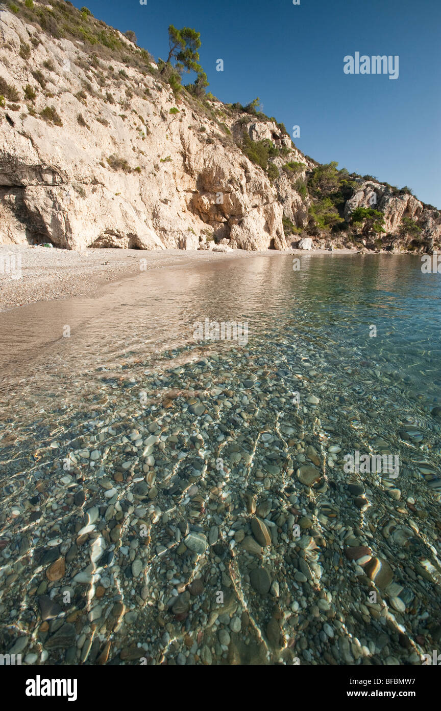 Crystal clear sea with small waves and a sandy beach with cliffs and rocks in the background on a greek island, Stock Photo