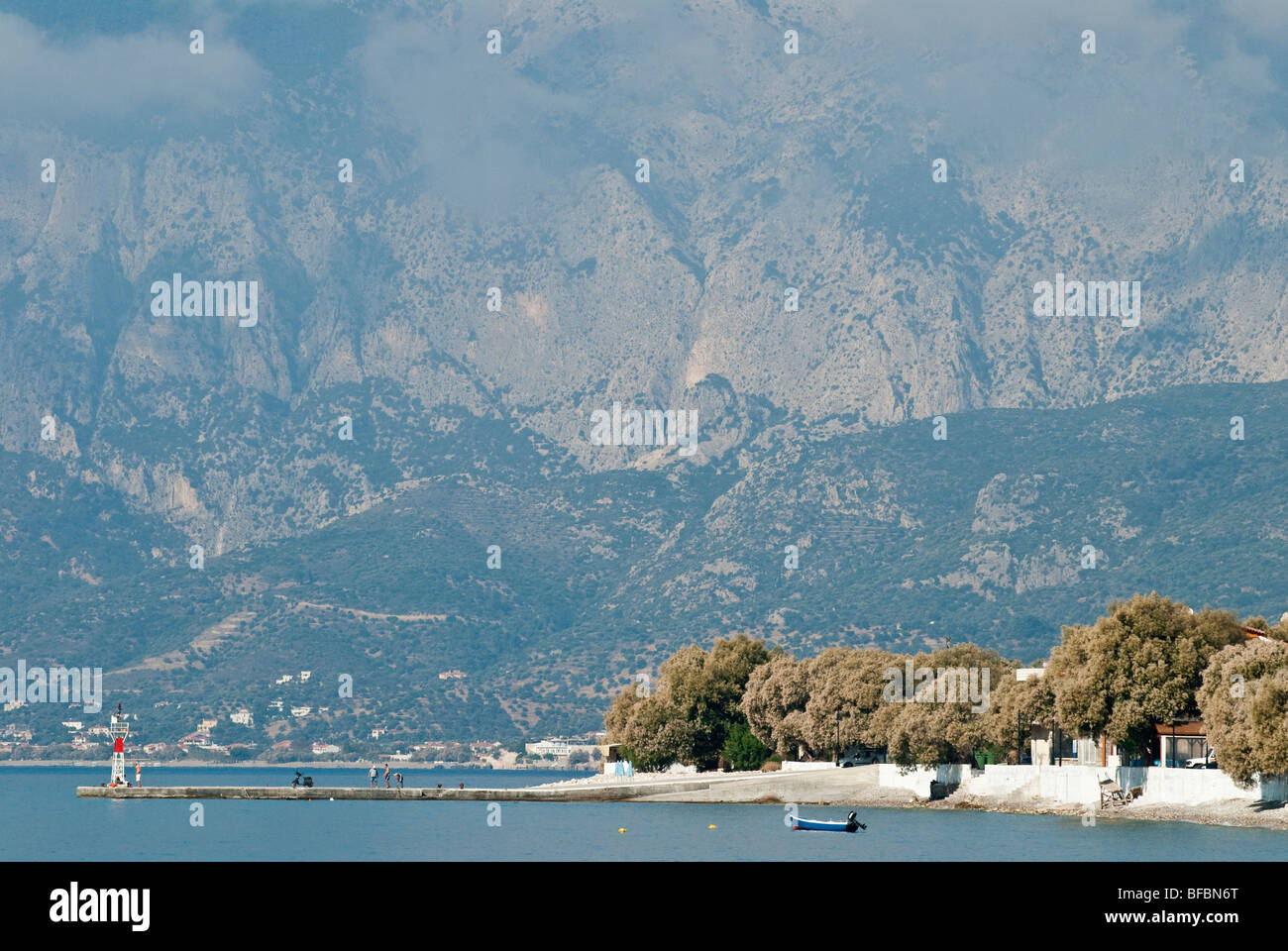 view across the sea to a beach and Tamarisk trees and steeply rising falnks of a huge montain in the background. Stock Photo