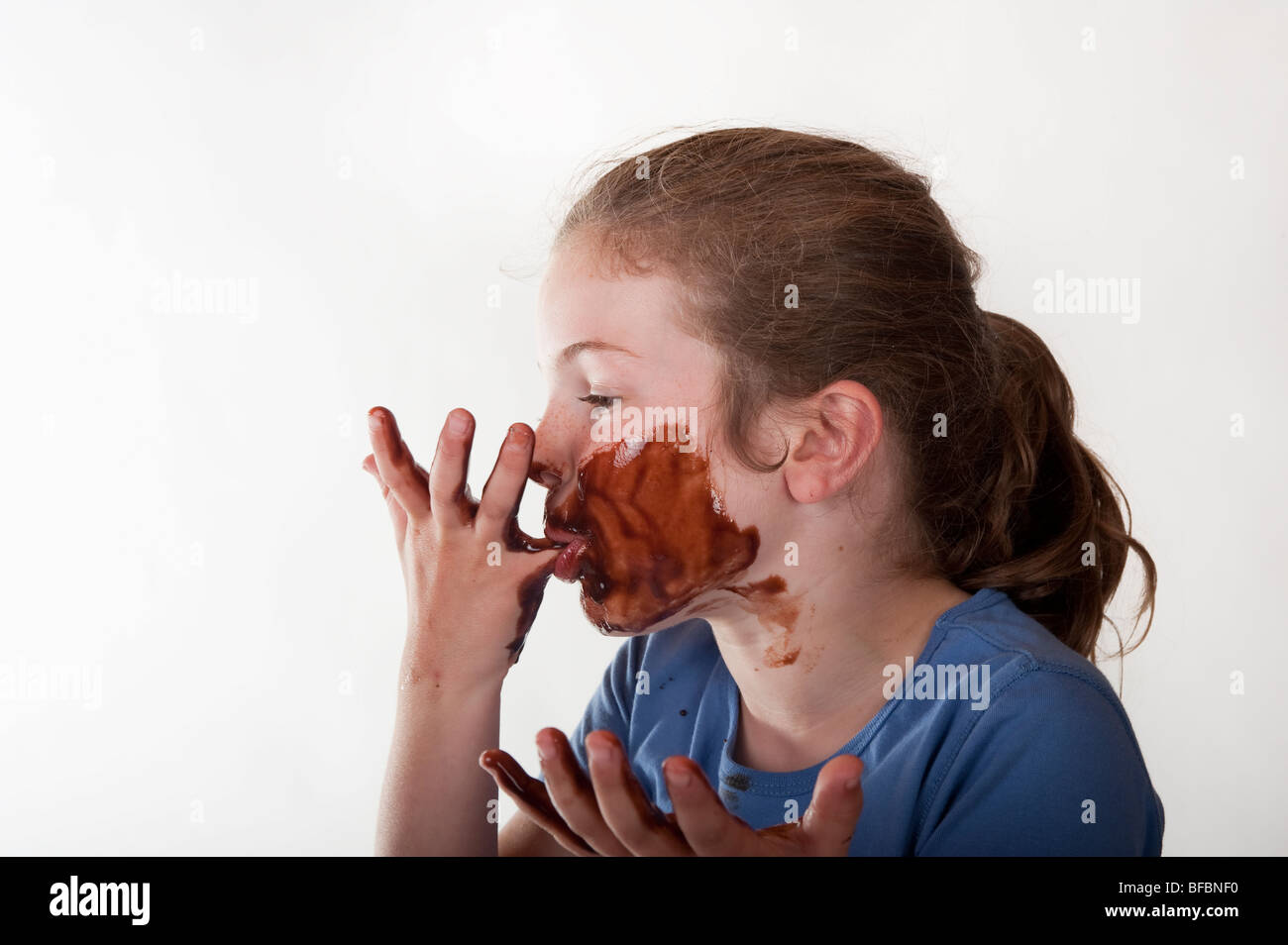 little girl with chocolate covered face and licking fingers Stock Photo