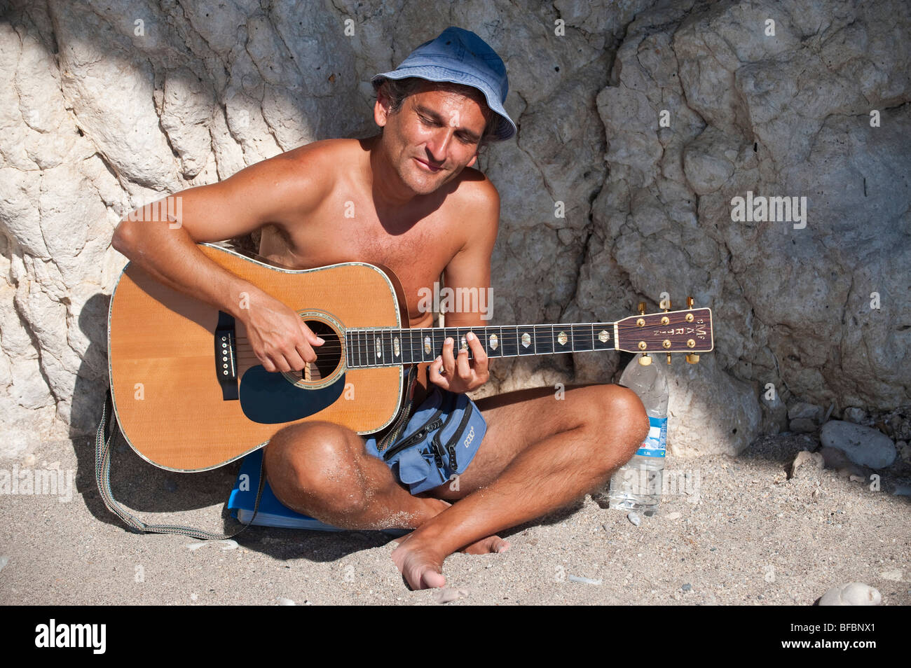 Guitar player sitting in the sun and playing his guitar on a greek island Stock Photo