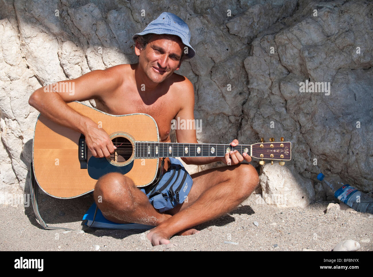 Guitar player sitting in the sun and playing his guitar on a greek island Stock Photo