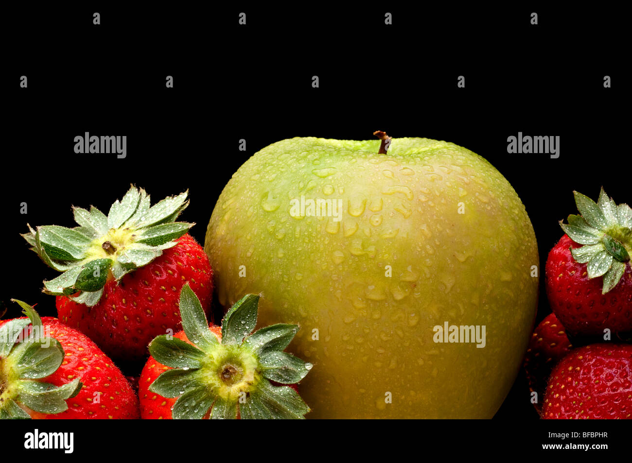 A green apple and red strawberries on black Stock Photo