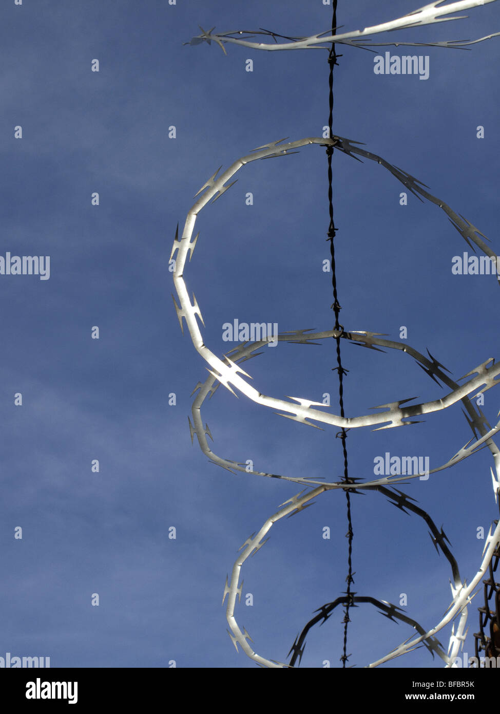 Rolled razor wire on top of a fence in New York City reflects the sunlight against a deep blue sky Stock Photo