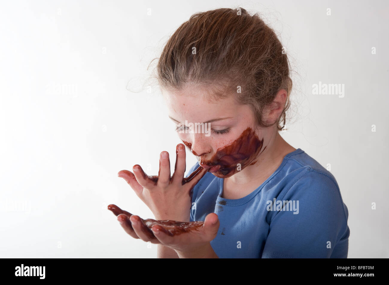 little girl with chocolate covered face licking her fingers Stock Photo
