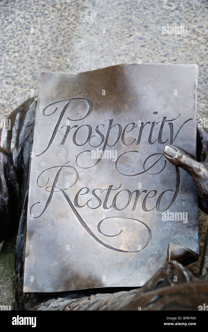 Close-up of a bronze statue showing a man holding a piece of paper with the words ' Prosperity Restored ' written on it. Stock Photo