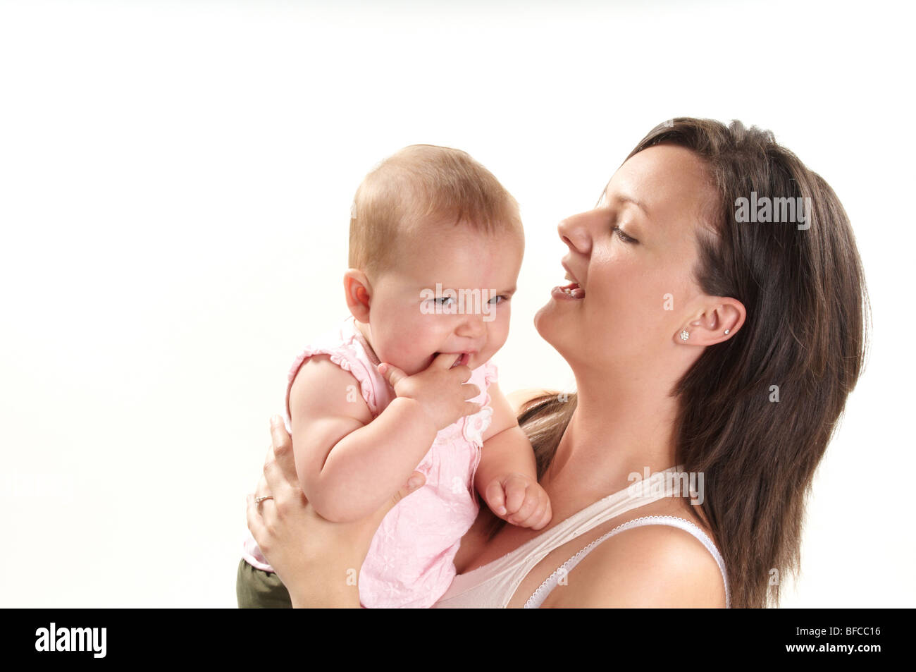 Brunette mum plays with blonde baby daughter on white background. twenty something mum and one year old little girl Stock Photo