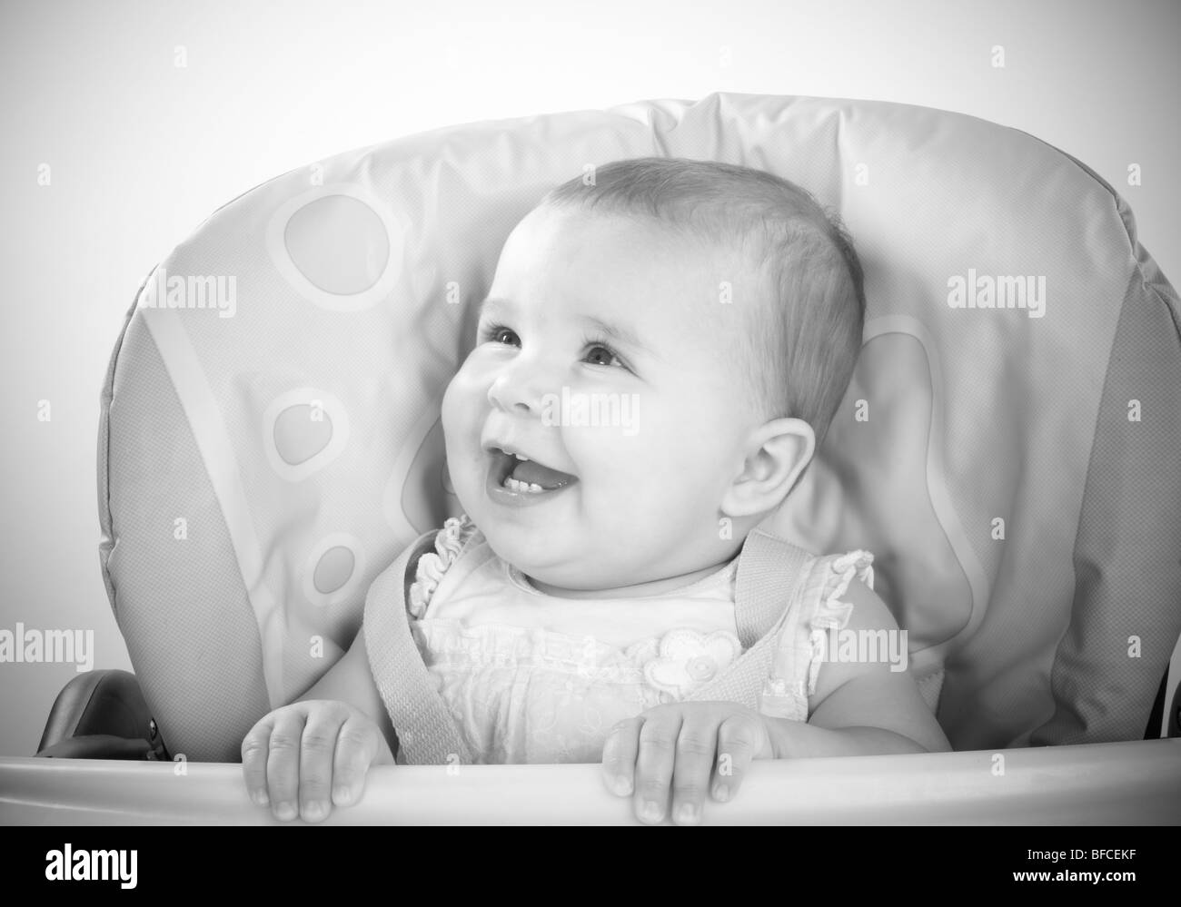 Baby Girl in pink top feeding and being fed in blue and yellow high chair Stock Photo