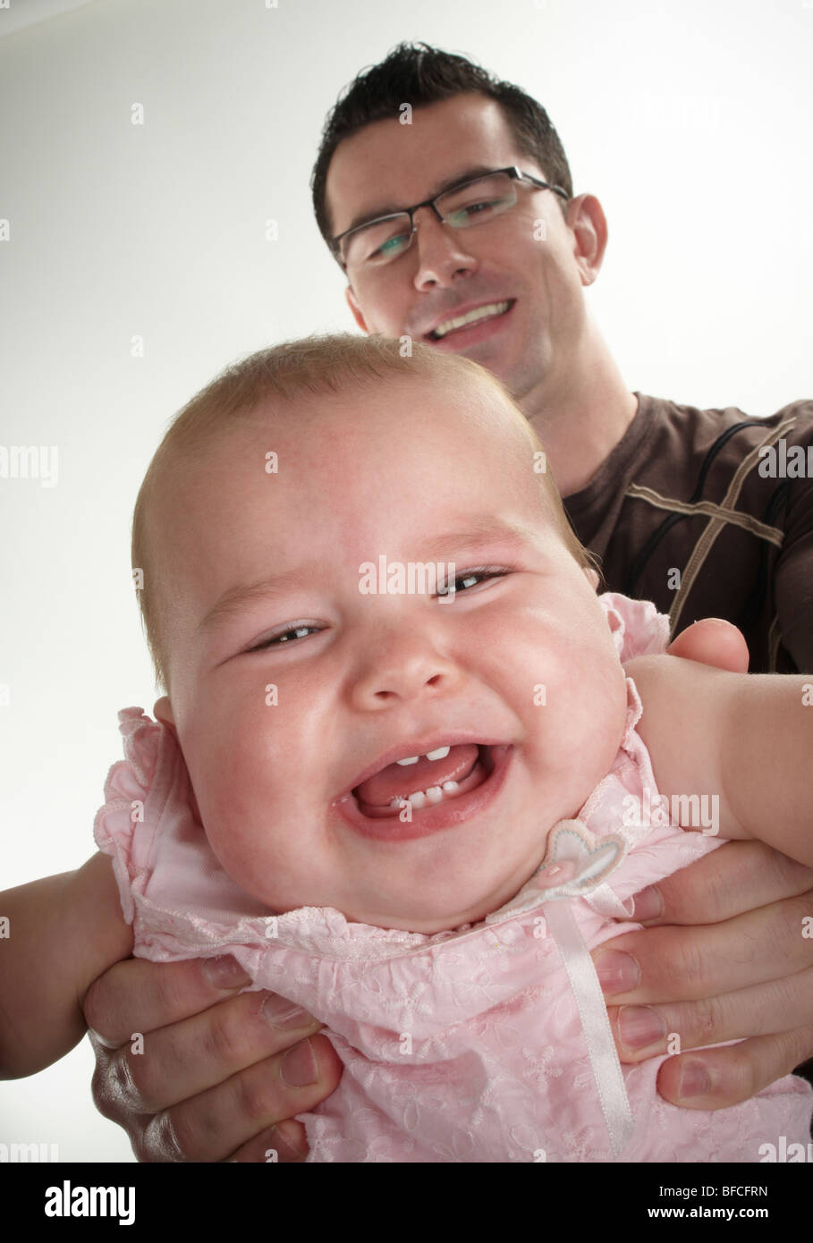 Dad holding baby daughter at arms length, daughter crying with laughter Stock Photo