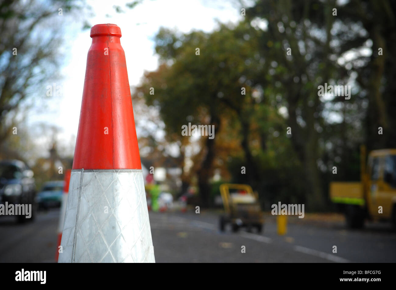 A red and white traffic cone placed in the middle of a UK road whilst routine maintenance is carried out. Stock Photo