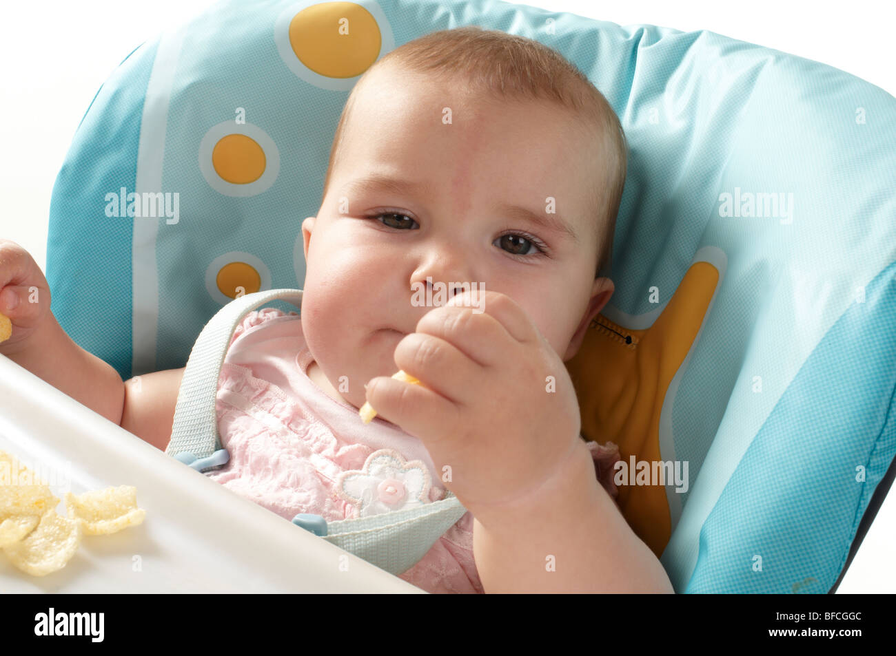 Baby Girl in pink top feeding and being fed in blue and yellow high chair Stock Photo