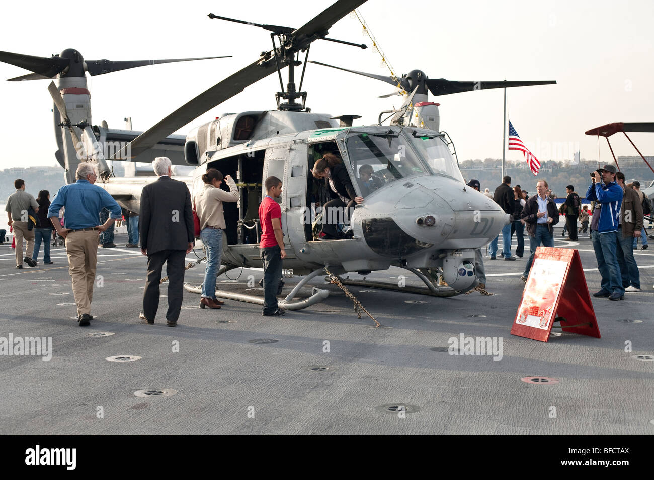 visitors admire a Marine Corps Huey helicopter sitting on the flight deck of the USS New York as woman clambers out of cockpit Stock Photo