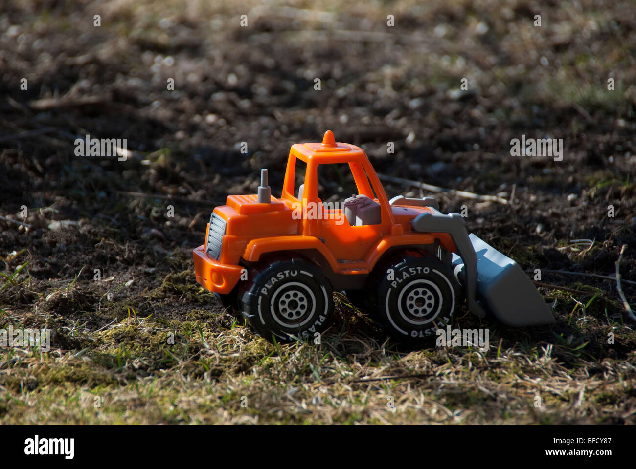 A plastic orange toy tractor on ground Stock Photo