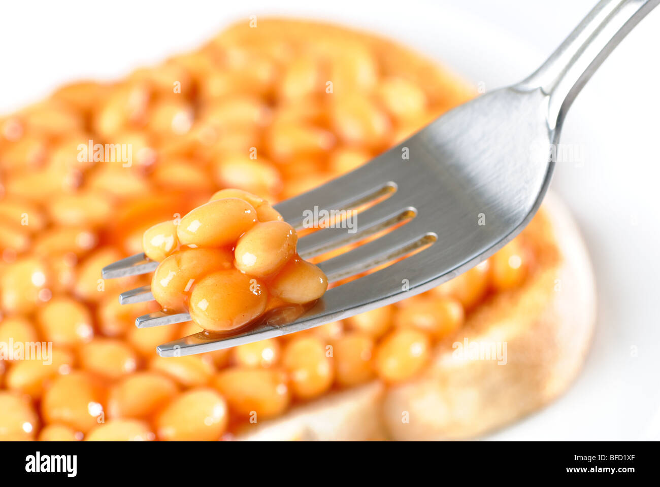 Fork of baked beans with beans on toast in background Stock Photo