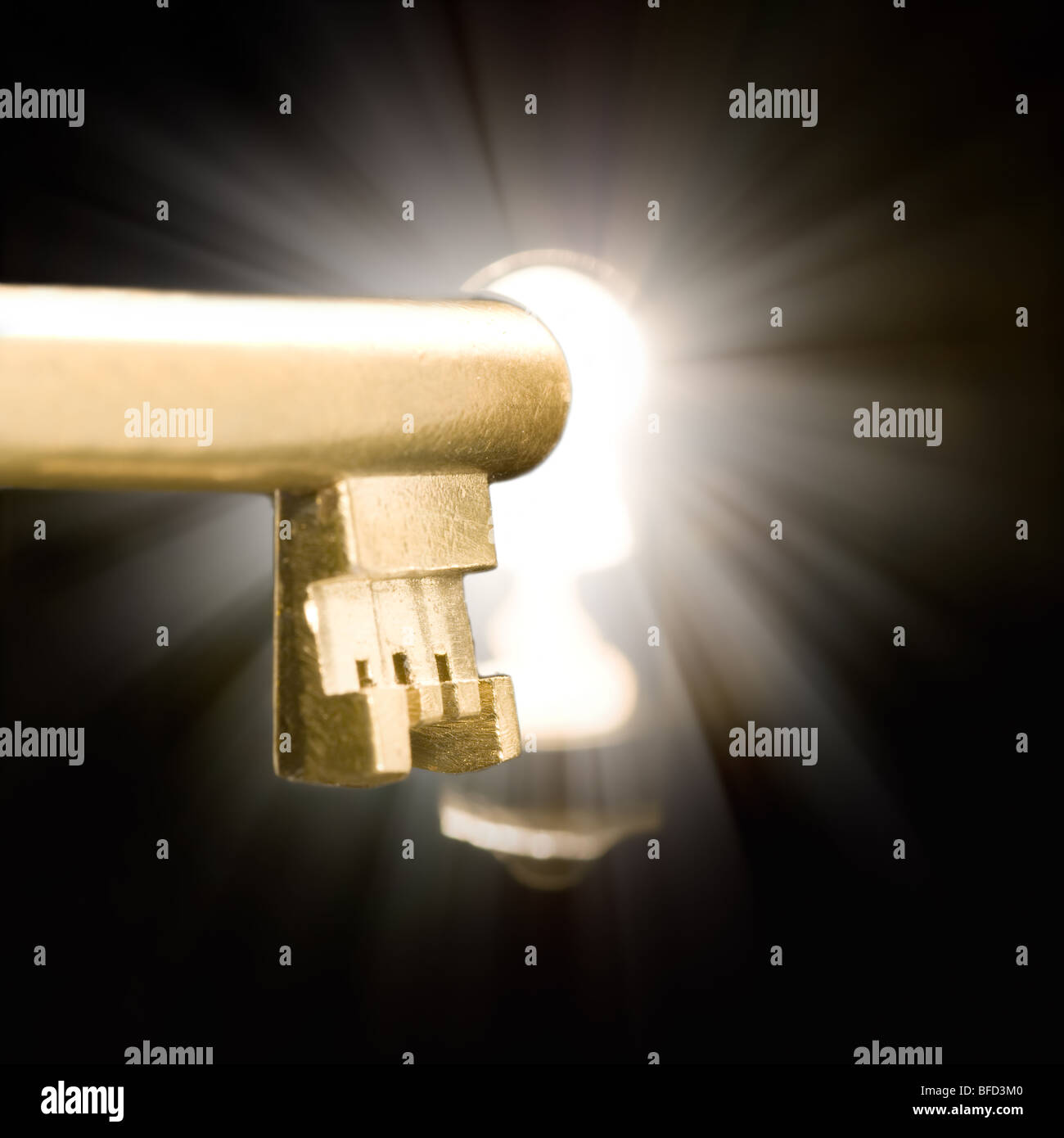 A golden key in a keyhole illuminated by a mysterious light coming from the other side. Stock Photo