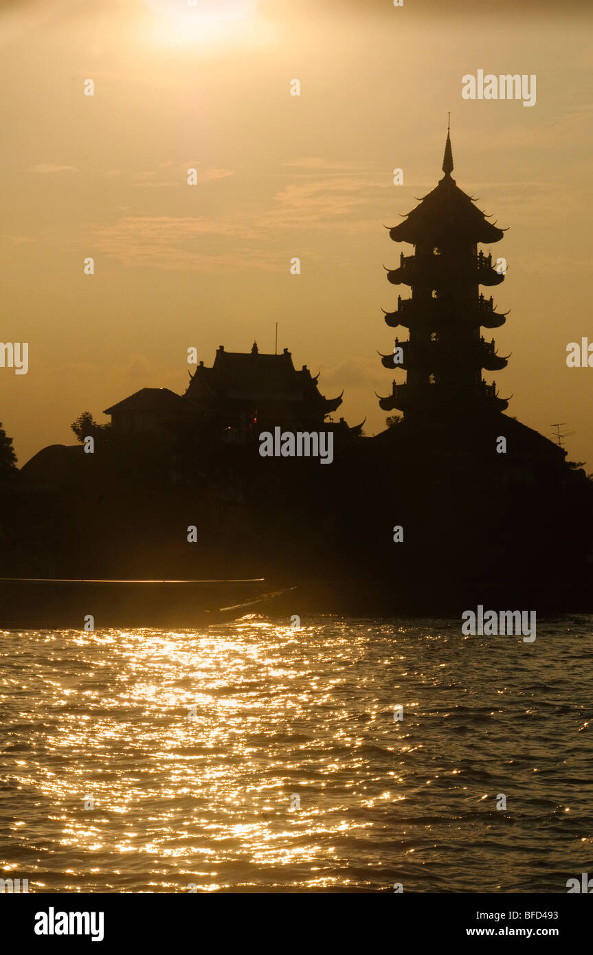 temple silhouetted at sunset along the Chao Phraya River in Bangkok ...