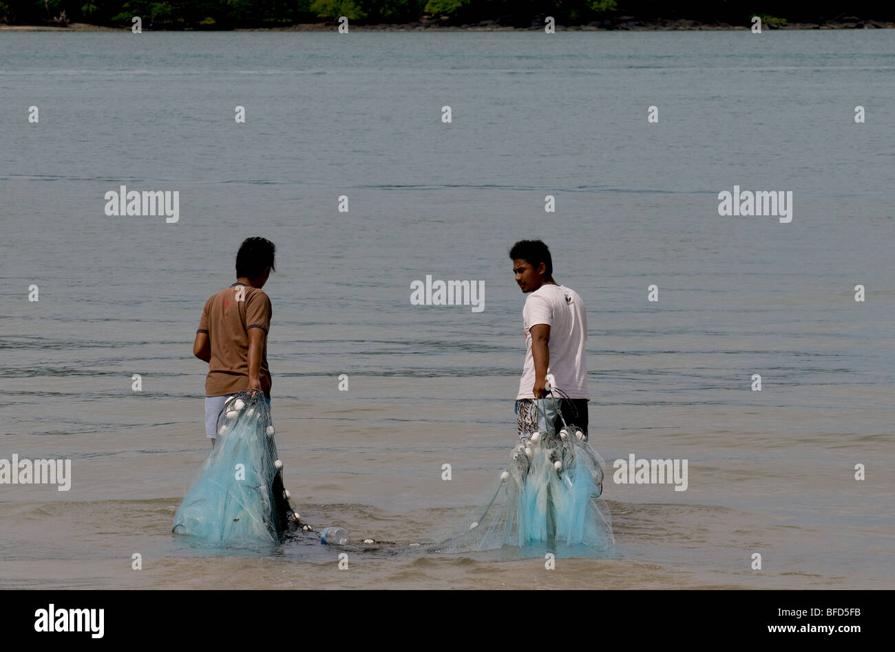 Two fishermen dragging a fishing net into the sea at Pantai Tengah