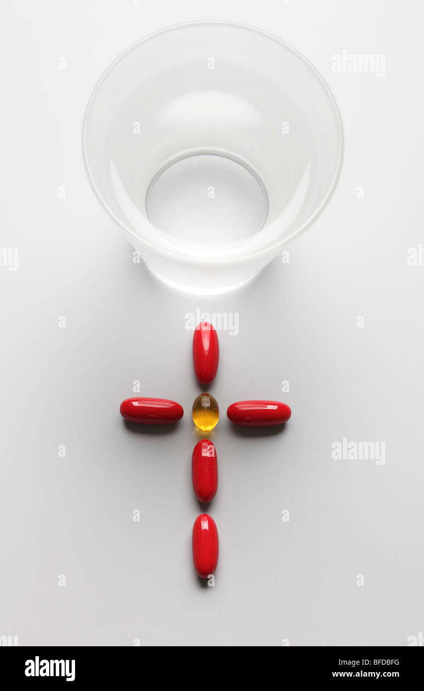 pills forming a cross next to a glass of water Stock Photo