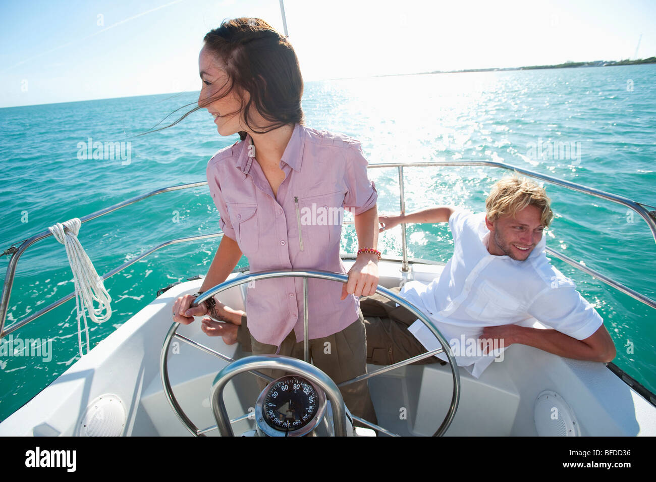 A woman pilots a boat off of Florida while a man sits nearby Stock