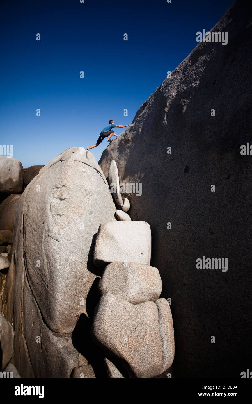 A man stretches out to explore atop giant boulders on the beach in The Baths National Park, Virgin Gorda. Stock Photo