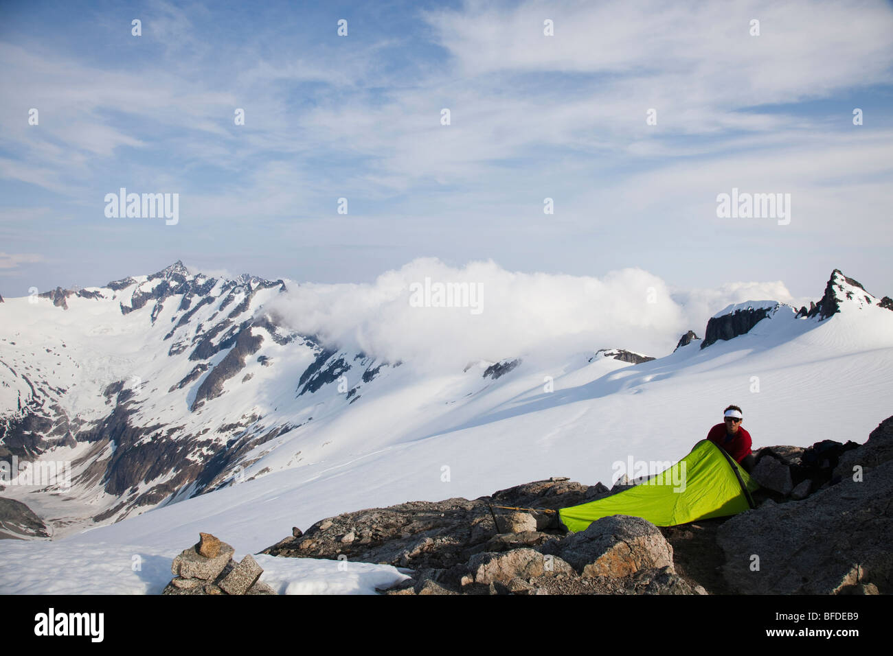 A young man sets up his bivy sac on a rock outcrop on a glacier while