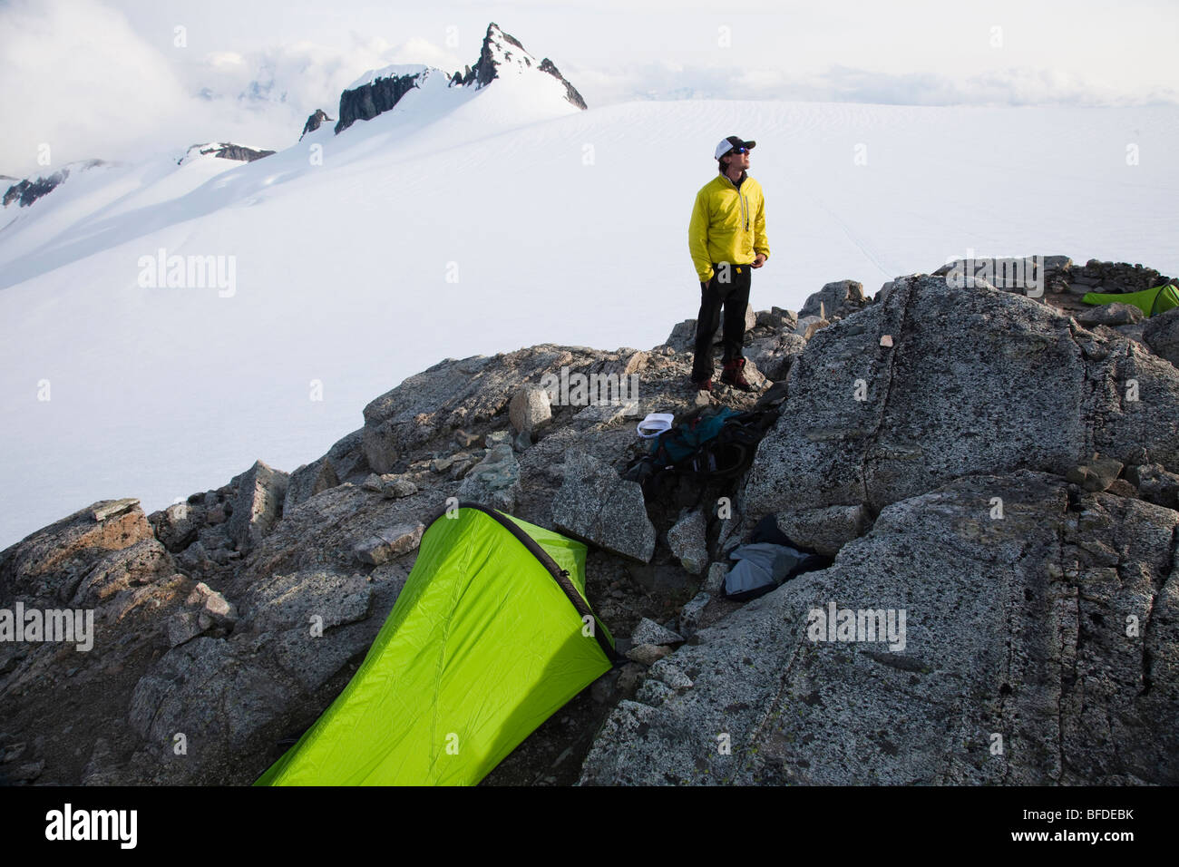 A young climber stands on a rock outcrop near his tent while climbing on a glacier in the mountains. Stock Photo