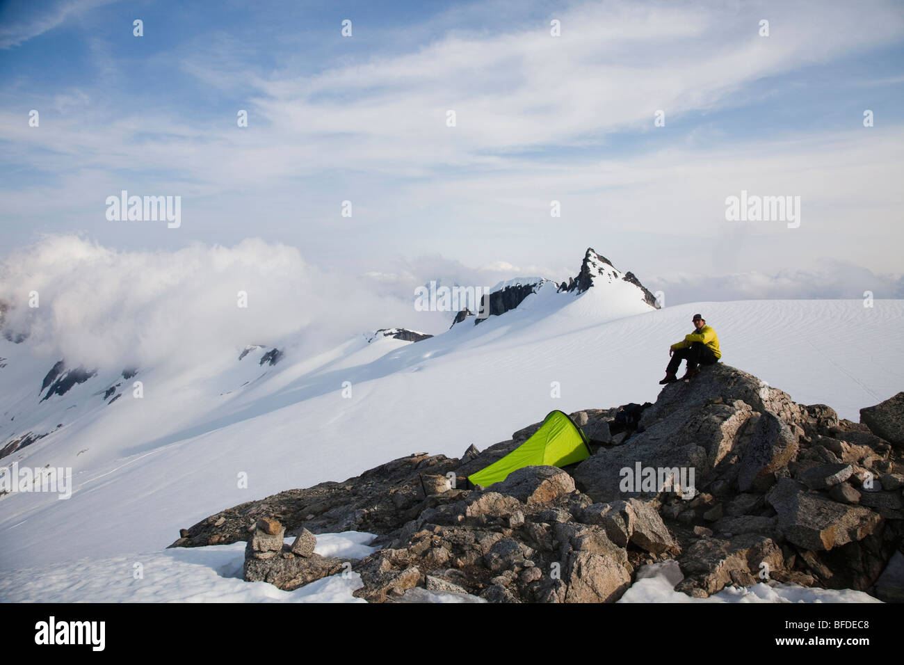 A young climber sits on a rock outcrop near his tent while climbing on a glacier in the mountains. Stock Photo