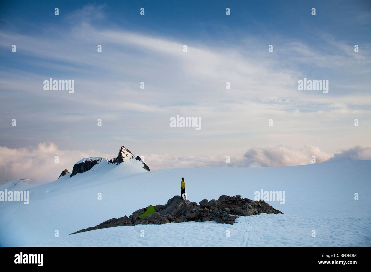A climber stands on a rock outcrop in the middle of a glacier while climbing in the North Cascades, WA. Stock Photo