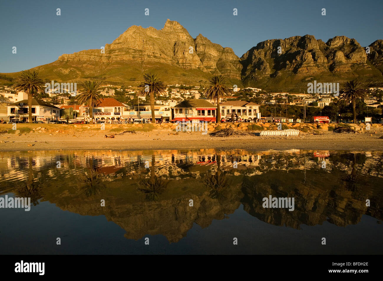 Sunset forms a reflection of the suburb of Camps Bay and the Twelve Apostles Mountain Range on the beach in Cape Town, South Afr Stock Photo
