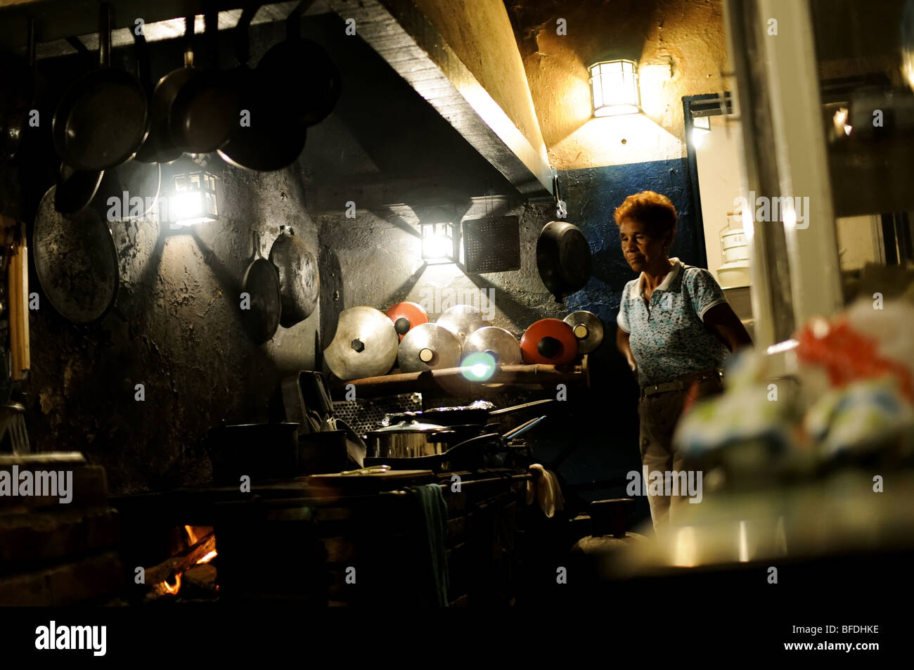 An elderly woman watches a wood-burning stove in a hacienda-style kitchen in Choroni, Venezuela. Stock Photo