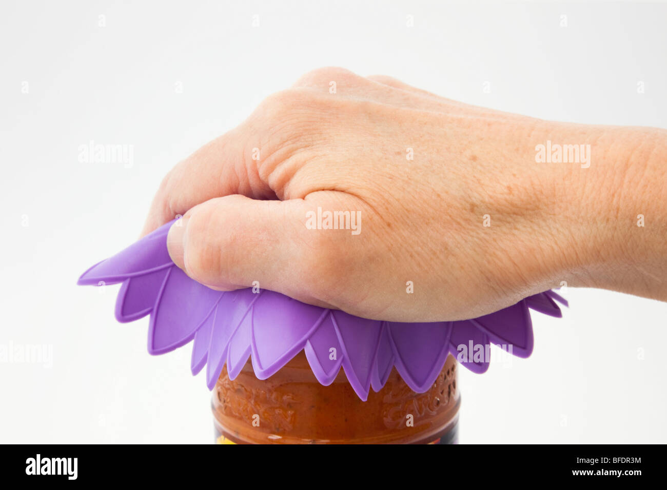 Mature person's hand twisting open a food jar using a silicone rubber trivet to take the top off. England UK Stock Photo