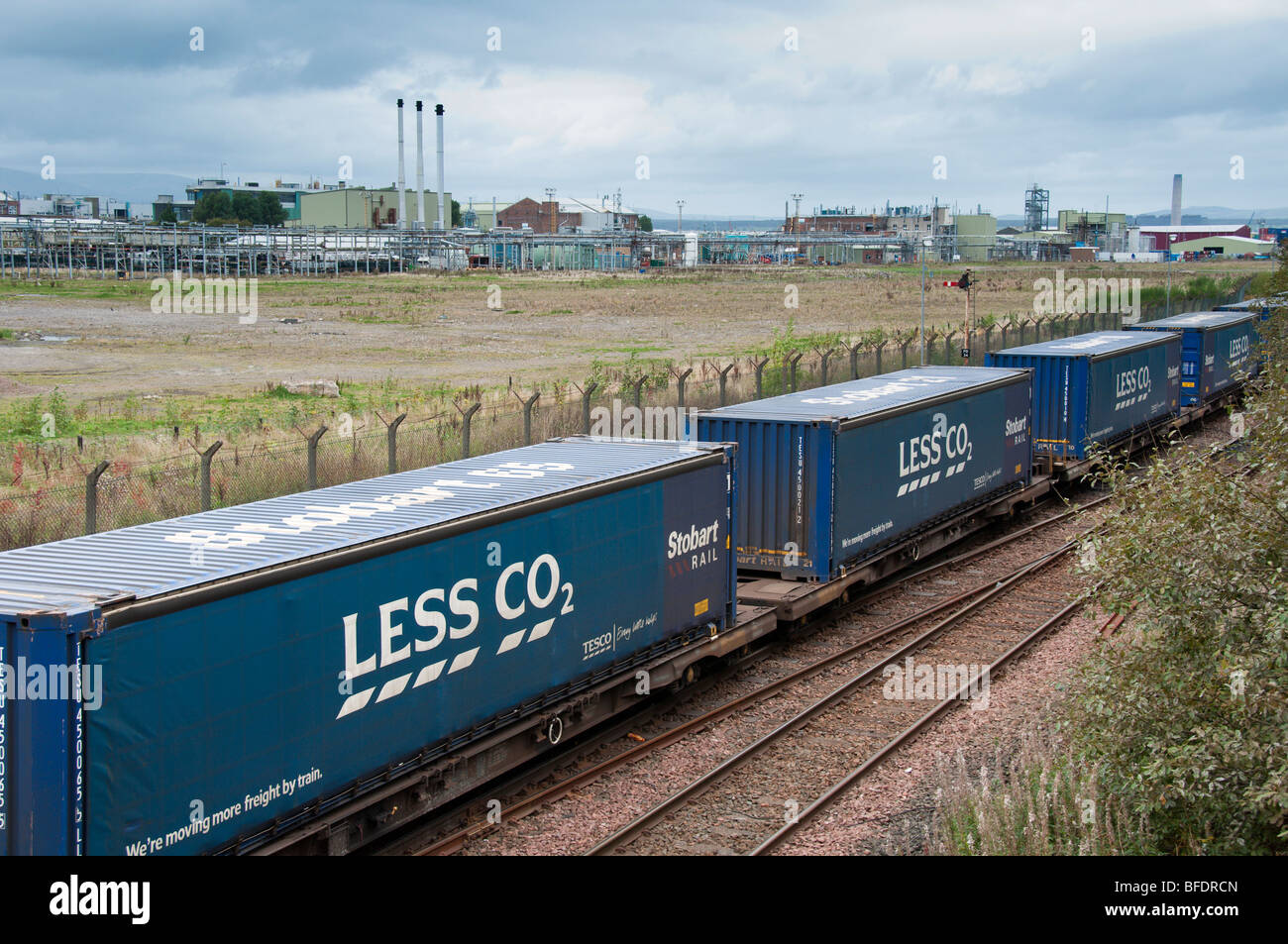 Tesco rail transport containers for supermarket goods with Less CO2 label at Grangemouth in Scotland with industry in background Stock Photo