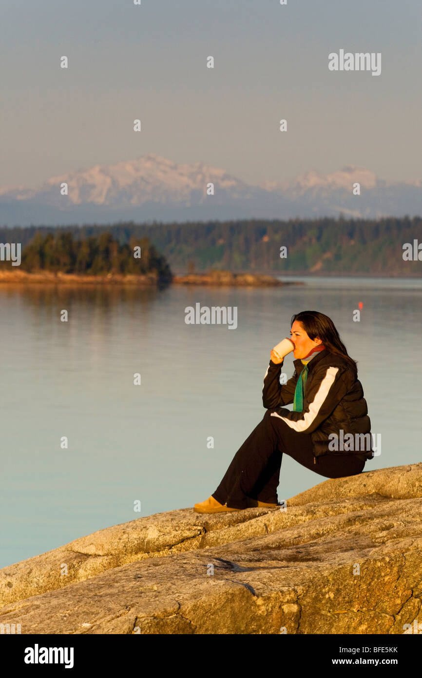 Woman savours her coffee in morning on bluffs overlooking Georgia Strait  on Cortes Island Gulf Islands British Columbia Canada Stock Photo