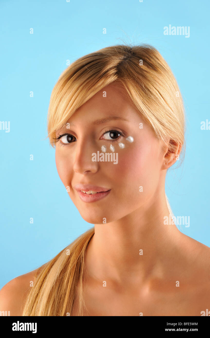 Blond girl with facial care cream on the ring under the eye Stock Photo