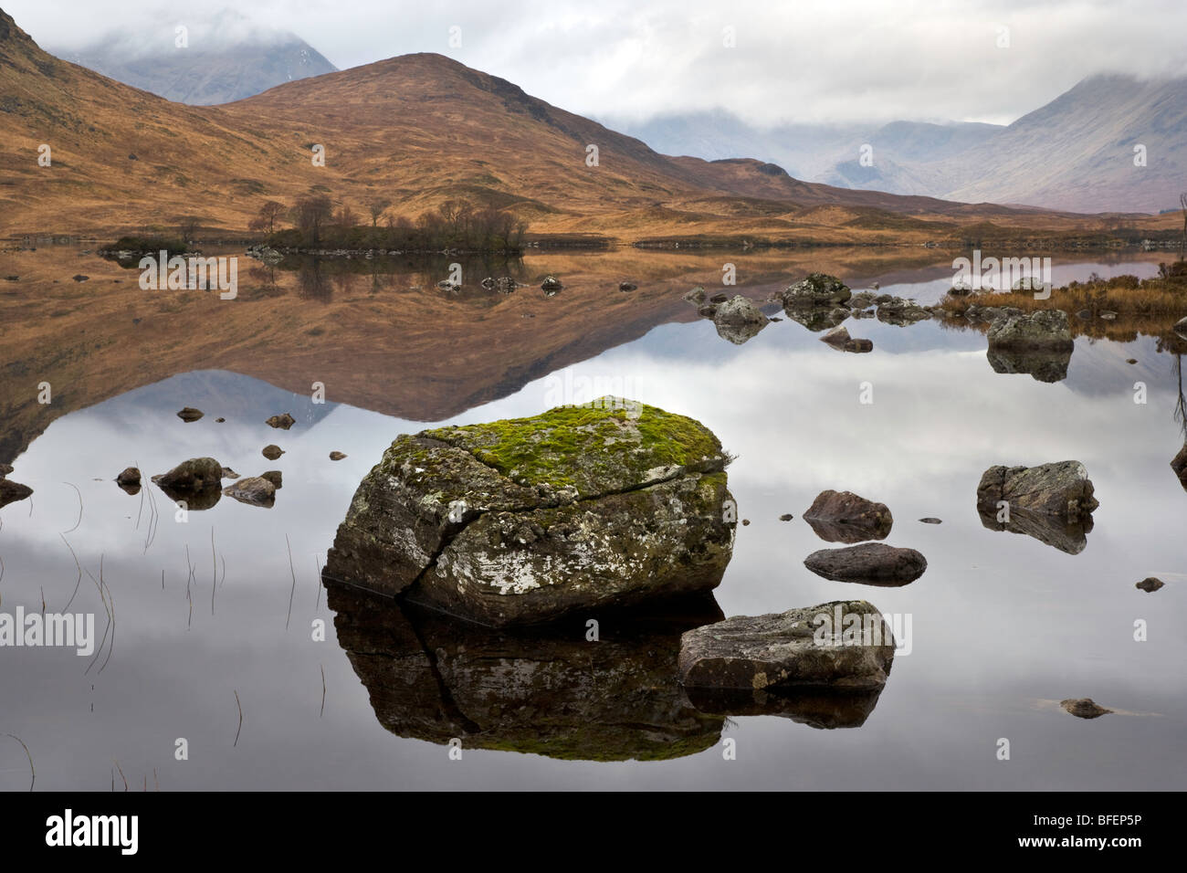 A huge boulder sits in a very still  Lochan Nah Achlaise on Rannoch  Moor in the Highlands of Scotland. Stock Photo