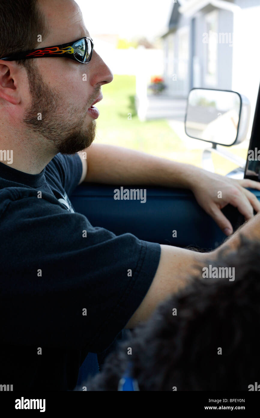 Inside the cab view of a man driving a pickup truck wearing sunglasses