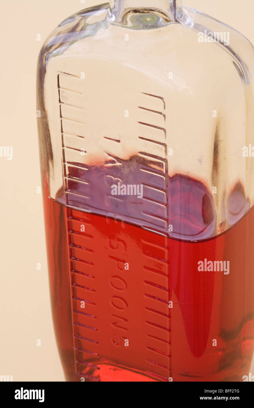 Studio Still life. Old glass medicine bottle with graduation marks for for measuring tablespoons half full containing red liquid Stock Photo