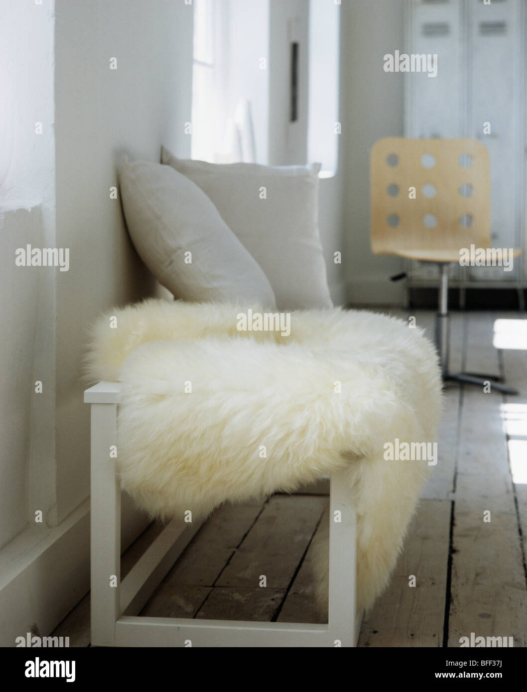 Close-up of cream sheepskin rug on cream wooden bench with grey cushions in modern living room Stock Photo