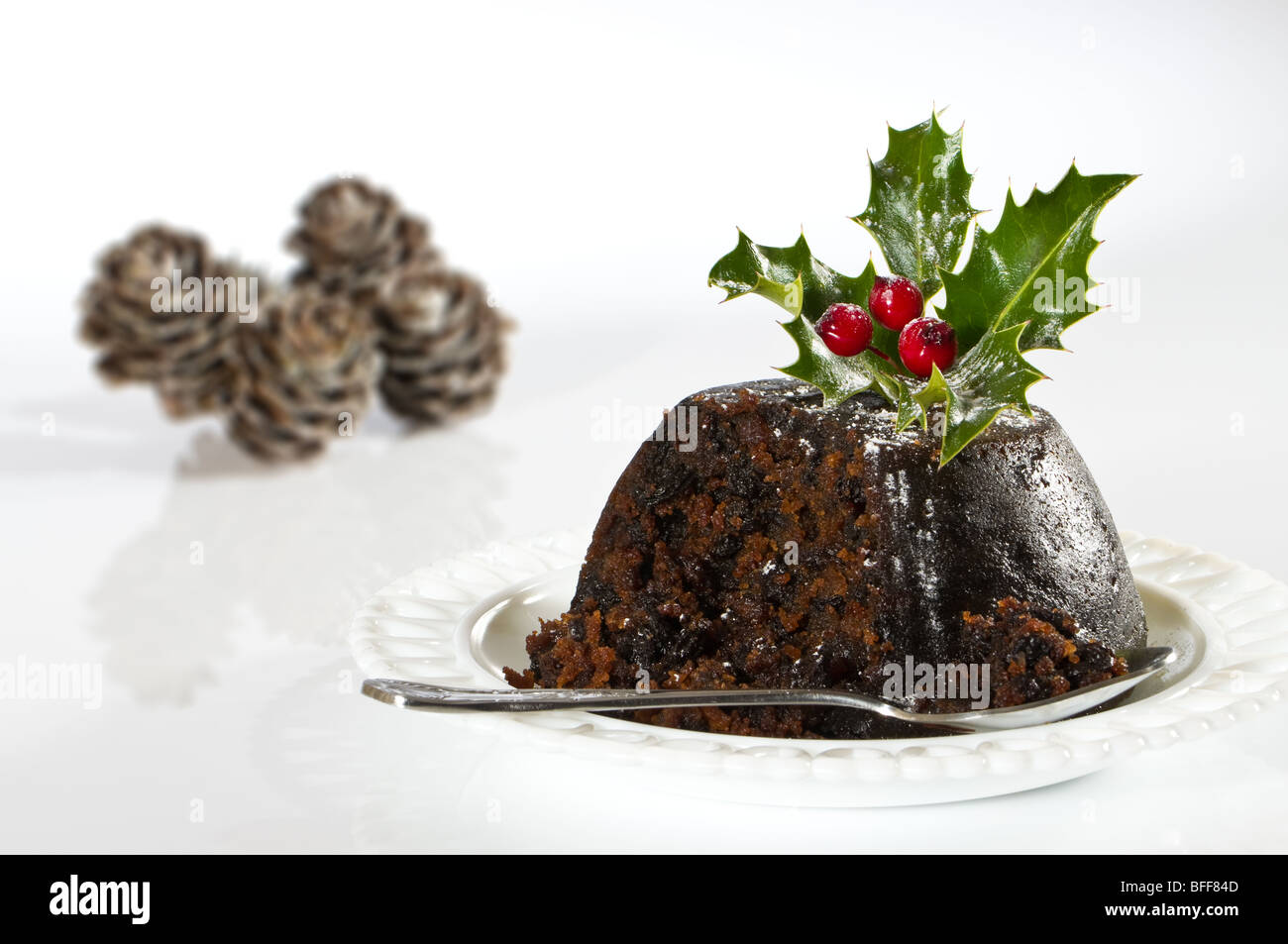 Christmas pudding with holly, cones in background Stock Photo