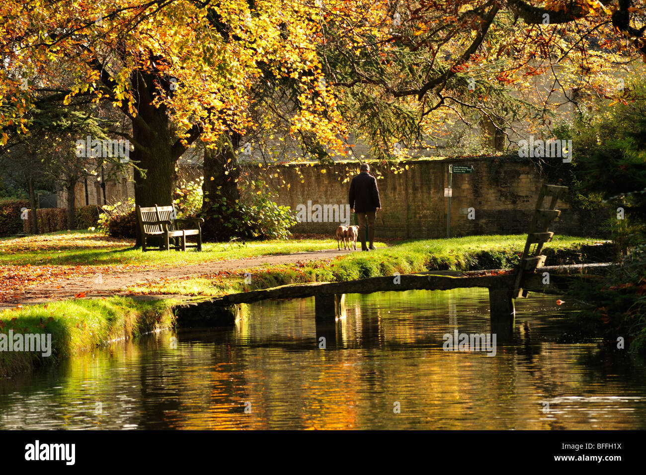 Dog walker by footbridge at Lower Slaughter in the Cotswolds in the Autumn, England, UK Stock Photo