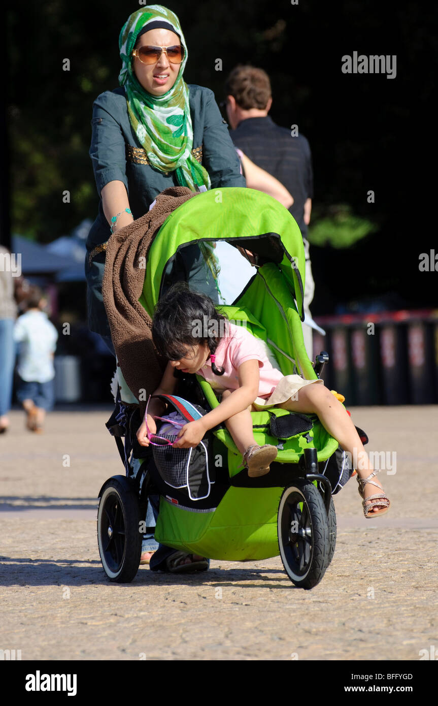 Islamic mother living in a multicultural country. A young woman in hijab with her child in a pram / buggy / pushchair. Stock Photo