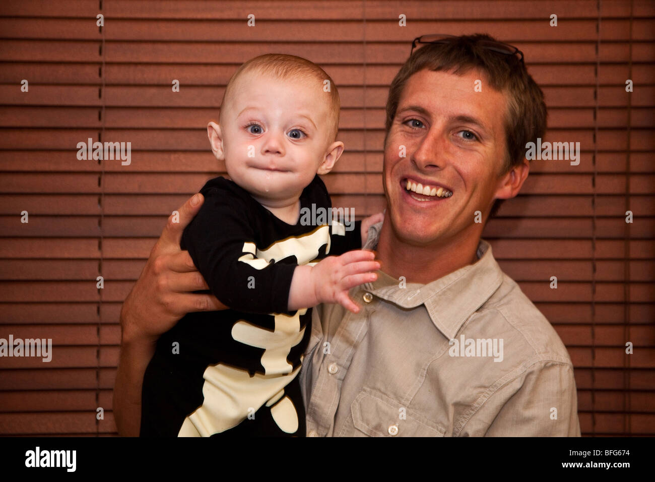 Happy baby boy (six months) in a skeleton outfit  with uncle in front of a wooden blind. London, England. Stock Photo