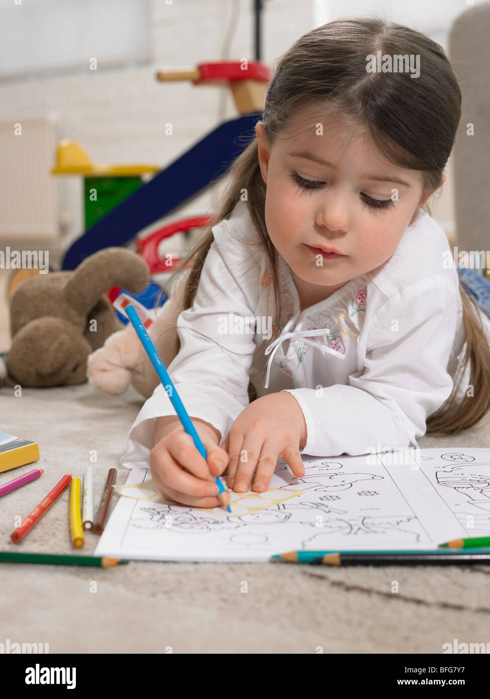 Girl (3-4) with colouring book on floor in home Stock Photo