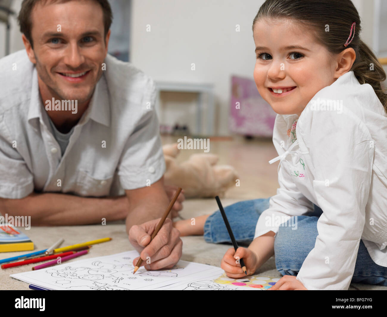 Father and daughter (3-4) colouring in book on floor, (portrait) Stock Photo